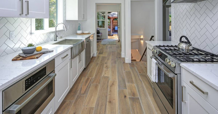 A newly remodeled kitchen features wide plank wood flooring with white cabinets and white countertops.