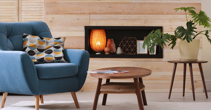 A blue armchair and a wooden coffee table sit in front of a faux fireplace accent wall in a cozy living room.