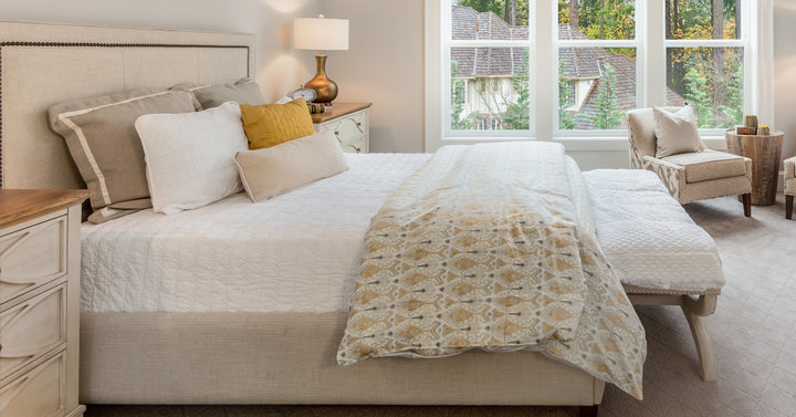 Sunlight shines through the window of a bright, yet cozy, master bedroom that features a vaulted ceiling with dark beams.