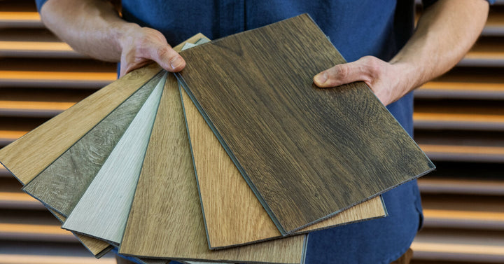 A person fans out a selection of luxury vinyl plank flooring while standing in front of a wall of organized samples.