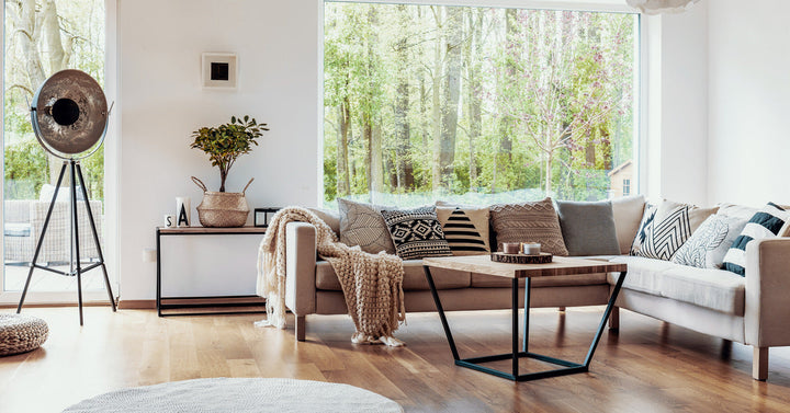 A tan sectional sofa sits in front of a large picture window in a living room with medium brown hardwood floors.