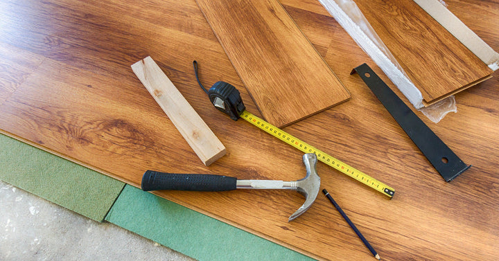 A hammer, tape measure, and a stack of flooring planks sit on top of a laminate wood floor that's partially installed.