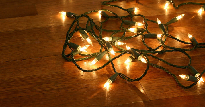 A tangled string of glowing Christmas lights highlight the glossy surface of a polished wooden floor.